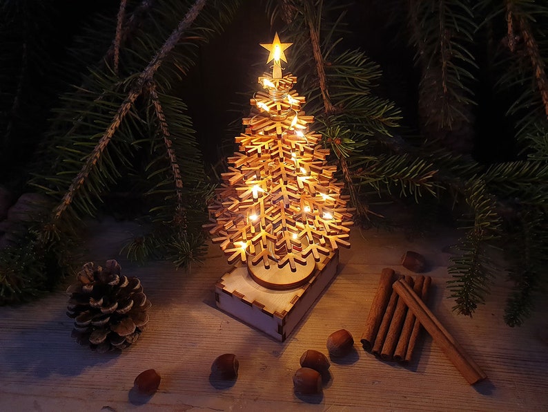 May include: A wooden Christmas tree with a star on top and warm white LED lights. The tree is on a wooden base and surrounded by cinnamon sticks and hazelnuts.