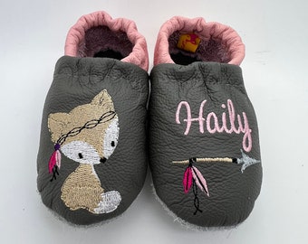 May include: Gray leather baby shoes with pink trim and a fox design embroidered on one shoe. The other shoe has the name "Haily" embroidered on it.