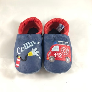 May include: A pair of blue leather baby shoes with red trim. One shoe has the name "Collin" embroidered on it, along with a fire hose and water spray. The other shoe has a red fire truck with the number "112" embroidered on it.