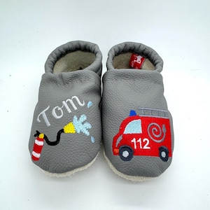Könnte beinhalten: Graue Lederschuhe für Babys mit einem gestickten Feuerwehrauto-Design auf einem Schuh und dem Namen "Tom" auf dem anderen Schuh.