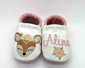 May include: White leather baby shoes with pink trim and a deer face embroidered on one shoe and the name "Alina" embroidered on the other shoe.