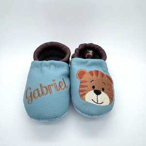 May include: A pair of light blue baby shoes with a tiger face embroidered on one shoe and the name "Gabriel" embroidered on the other shoe.