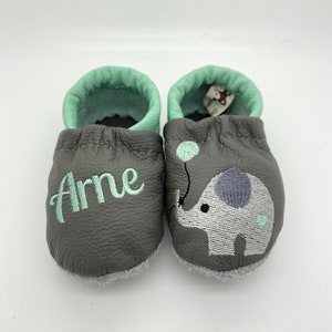 May include: Gray leather baby shoes with a green trim and an embroidered elephant with a balloon. The shoes are personalized with the name "Arne".