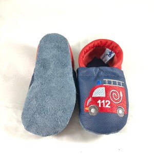 May include: A pair of blue leather baby shoes with a red fire truck embroidered on one shoe. The shoes have a soft suede sole.