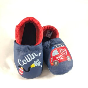 May include: Blue leather baby shoes with red trim. One shoe has the name "Collin" embroidered on it, and the other shoe has a red fire truck with the number "112" embroidered on it.