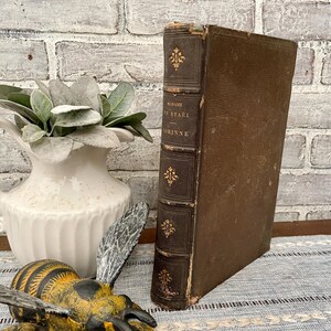 May include: A vintage brown leather-bound book with gold lettering on the spine. The title is "MADAME DE STAEL CORINNE".