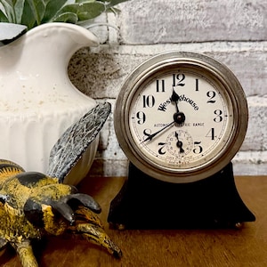 May include: A round Westinghouse electric clock with a silver-toned metal bezel and a black base. The white clock face features black Arabic numerals, black hands, and a smaller sub-dial. Text on the face reads Westinghouse, AUTOMATIC ELECTRIC RANGE, and CLOCK STYLE 32763.