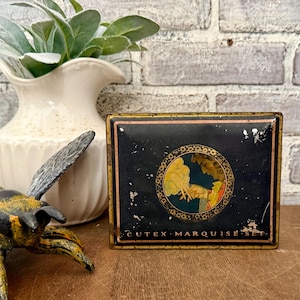 May include: A vintage black and gold Cutex Marquise Set tin. The tin features a circular illustration of a person in a yellow and red outfit. The text "CUTEX MARQUISE SET" is printed on the bottom of the tin.