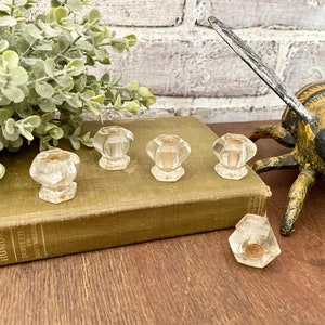 Peut inclure: Six boutons de cabinet en verre transparent avec un design facetté. Les boutons sont disposés sur un livre vert avec le titre "American Wit and Humor" visible. Les boutons sont sur une surface en bois avec une figurine d'abeille décorative.