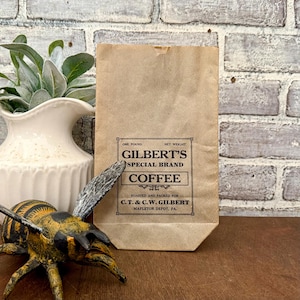 以下が含まれることがあります： 「One Pound」と「Roasted and Packed for C.T. & C.W. Gilbert, Mapleton Depot, PA.」の文字が入った、Gilbert's Special Brand Coffeeの茶色の紙袋。 袋は直立しています。