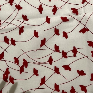 Könnte beinhalten: Weißer Stoff mit einem sich wiederholenden Muster aus roten Blütenformen und dünnen, gebogenen Stielen. Das Design ist gleichmäßig verteilt und erzeugt eine zarte und organische Ästhetik. Der Stoff scheint Baumwolle oder ein ähnliches Material zu sein.