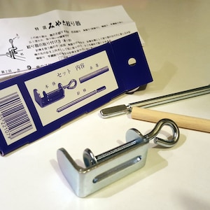 Op de afbeelding: Een blauwe doos met een zilveren klem, een houten pen en een metalen staaf. De doos heeft Japanse tekst die "Set-inhoud" en een barcode zegt. De tekst op de doos zegt ook "Speciale selectie Miyako Tie-Dye Tool".