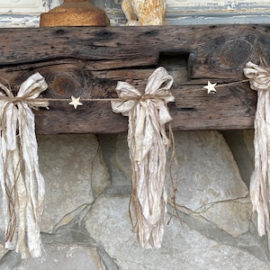 May include: A rustic wooden mantelpiece decorated with a garland of white fabric bows and small wooden stars.