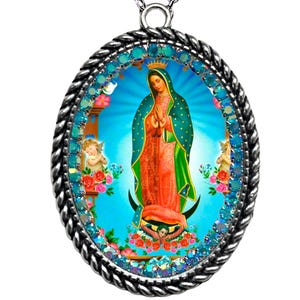 Pode incluir: Colar com pingente oval apresentando uma imagem de Nossa Senhora de Guadalupe. O pingente tem uma borda prateada em forma de corda e uma borda de pedras preciosas turquesa. A imagem retrata a Virgem Maria com uma capa verde-azulado e um vestido laranja, com anjos e rosas.