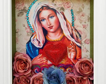 Könnte beinhalten: Ein gerahmtes Bild der Jungfrau Maria, die ein rotes Herz mit einem floralen Rand hält. Der Rahmen ist mit getrockneten Rosen und einer blauen Blume verziert.