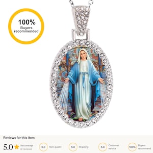 Puede incluir: Collar con colgante plateado con un colgante ovalado que representa una figura religiosa con túnica azul, rodeada de cristales transparentes. El colgante cuelga de una cadena plateada. La imagen está enmarcada por un borde de cristal y una fianza con cristales.