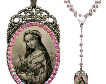May include: A silver-toned rosary necklace with a pink crystal pendant featuring a vintage image of a saint. The pendant is surrounded by a border of pink crystals.