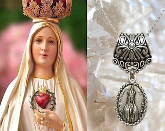 Può includere: Una statua di una donna con corona e veste bianca, che tiene un rosario e un cuore. Accanto, una collana con pendente in argento con un ciondolo ovale raffigurante una donna e le parole "N. S. DO ROSARIO DA FATIMA".