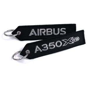 May include: Two black embroidered keychains with silver text. One keychain reads "AIRBUS", the other reads "A350 XWB". Each keychain has a silver metal ring attached for keys.