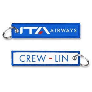 Puede incluir: Dos llaveros rectangulares. El superior es azul con el texto "ITA AIRWAYS" en blanco. El llavero inferior es blanco con el texto "CREW - LIN" en azul. Ambos tienen un llavero plateado.