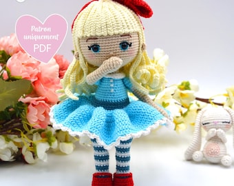 May include: A crocheted doll with blonde hair, a blue dress, and red shoes. The doll is holding her hands to her face. The doll is sitting on a white surface with a white crocheted bunny sitting behind it.