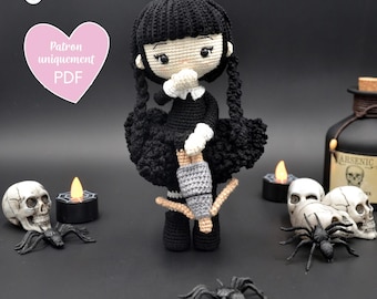 May include: A black crocheted doll with long black hair, wearing a black dress and holding a broom. The doll is surrounded by Halloween decorations, including skulls, spiders, and candles.
