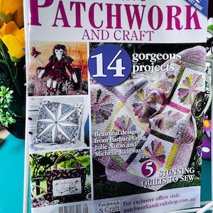 Puede incluir: Una revista titulada "Creative Patchwork and Craft" con el texto "14 gorgeous projects" y "5 stunning quilts to sew". La portada presenta imágenes de proyectos de patchwork, incluyendo colchas y un pequeño bolso. La revista está en un estante de alambre blanco.