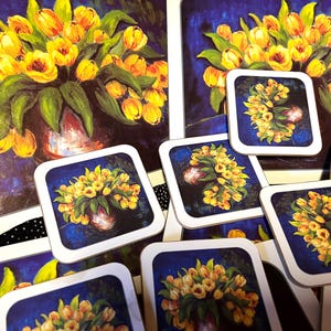 May include: A set of square coasters and a placemat with a floral design. The artwork depicts a bouquet of yellow tulips in a vase against a dark blue backdrop. The coasters have white borders, perfect for protecting surfaces from hot drinks.
