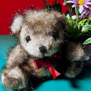 Puede incluir: Un oso de peluche marrón con una cinta roja alrededor del cuello. El oso tiene una cara marrón claro y una nariz negra. El fondo incluye flores coloridas. Un juguete clásico.