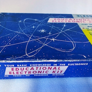 Op de afbeelding: Een vintage Eleco Educational Electronic Kit doos. De blauwe doos heeft witte ster- en lijnontwerpen, met roze en witte tekst. De kit bevat experimenten met zonnecellen en andere elektronische componenten. Geen gereedschap of solderen vereist.