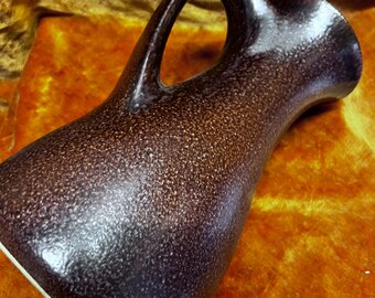 May include: A brown ceramic pitcher with a speckled finish and a large, arched handle. The pitcher has a wide base and a narrow spout. The interior is white. The overall shape is sleek and modern, suitable for serving beverages.