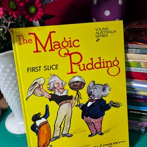 May include: A vintage children's book titled "The Magic Pudding" with a bright yellow cover. The cover features illustrations of cartoon characters, including a penguin, a man, and a koala. The book is part of the Young Australia Series.