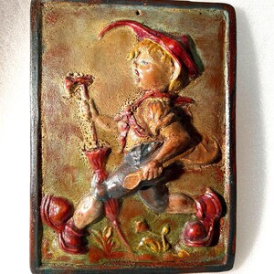 May include: A rectangular, relief-style wall plaque featuring a running figure in a red hat and boots, holding a staff. The figure is dressed in brown and blue clothing. The background is a textured, earthy tone with green and red accents.