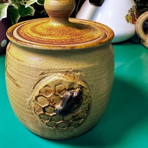 May include: A white ceramic mug with a black handle and the text "But First, Coffee" in a handwritten style. The mug is on a white surface. The mug is approximately 10 cm tall.