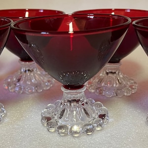 Könnte beinhalten: Sechs rote Dessertgläser aus Glas mit klaren Stielen und Böden. Die Böden haben ein perlenförmiges Design.