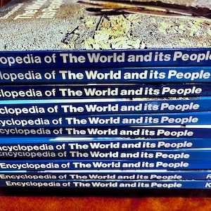 May include: A stack of blue hardcover books titled "Encyclopedia of The World and its People." The book spines are a vibrant blue with white lettering. The top of the stack shows a textured, gray surface.