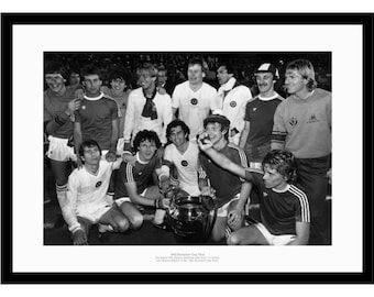 May include: A black and white photo of a soccer team holding a trophy. The team is wearing jerseys and shorts. The trophy is a large silver cup with a handle.