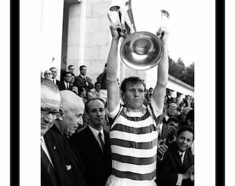 May include: Black and white photo of a man holding up a trophy. The man is wearing a striped jersey and is surrounded by other people. The text "1967 European Cup Final" is at the bottom of the photo.