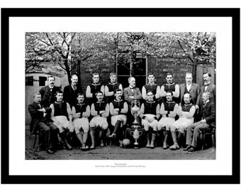 May include: Black and white photo of a soccer team, the Aston Villa 1897 League Champions and FA Cup Winners, posing with a trophy. The team is wearing uniforms and standing in front of a building.
