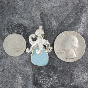 May include: Silver octopus pendant with a blue opal stone. The octopus has green eyes and is holding the opal stone. The pendant is about the size of a quarter.