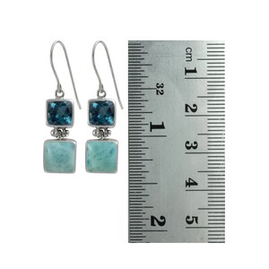 May include: Sterling silver dangle earrings with a blue topaz and a blue green gemstone. The earrings are approximately 2 cm long.