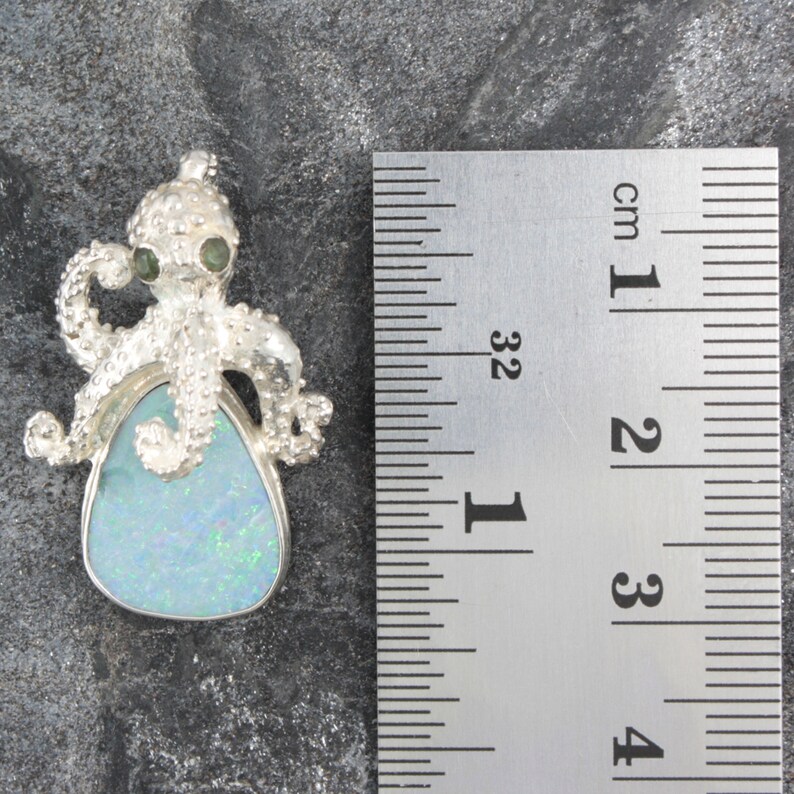 May include: Silver octopus pendant with a blue opal gemstone. The octopus has green eyes and is about 2 cm in size.