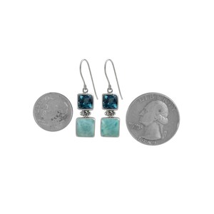 May include: Sterling silver dangle earrings with two square gemstones. The top stone is a deep blue topaz and the bottom stone is a light blue aquamarine. The earrings are shown next to a US quarter for size reference.