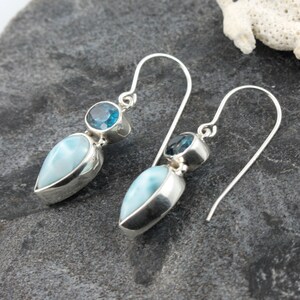 May include: A pair of silver dangle earrings with blue and white gemstone drops. The earrings feature a teardrop-shaped blue gemstone and a round blue gemstone.