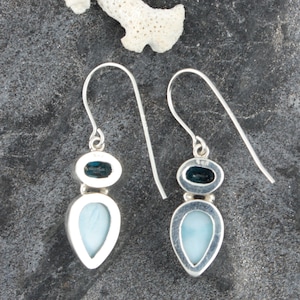 May include: A pair of silver dangle earrings with a teardrop-shaped blue lace agate gemstone and a smaller oval-shaped blue topaz gemstone.