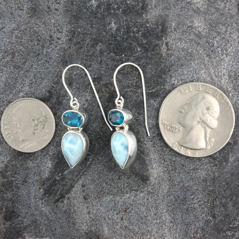 May include: Sterling silver dangle earrings with a teardrop shaped blue lace agate gemstone and a smaller round blue topaz gemstone. The earrings are shown next to a US quarter for size comparison.