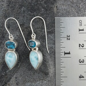 May include: Sterling silver dangle earrings with a teardrop shaped blue lace agate gemstone and a smaller oval shaped blue topaz gemstone. The earrings are approximately 2 inches long.