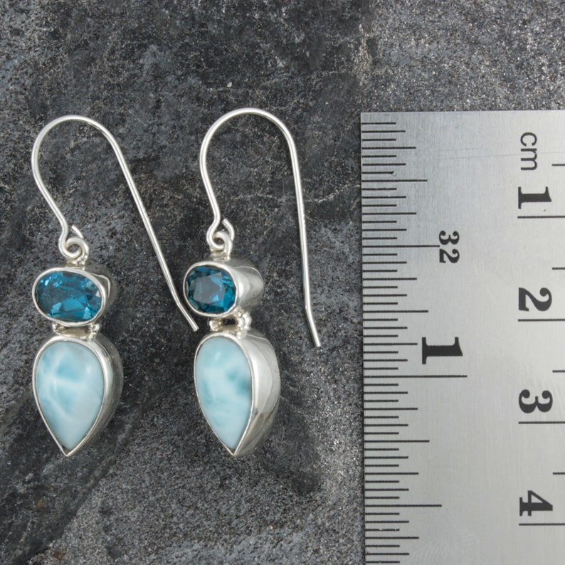 May include: Sterling silver dangle earrings with a teardrop shaped blue lace agate gemstone and a smaller oval shaped blue topaz gemstone. The earrings are approximately 2 inches long.
