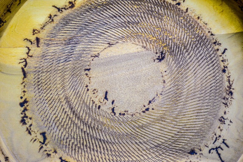 Puede incluir: Vista de cerca de un dise&ntilde;o circular abstracto con un patr&oacute;n en espiral. El centro es de color beige claro, rodeado de l&iacute;neas conc&eacute;ntricas en gris oscuro y negro. Los bordes exteriores tienen un tono amarillo-beige con acentos oscuros.