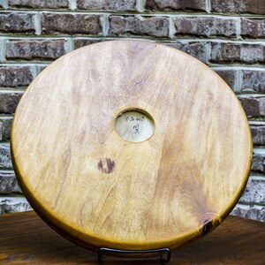 Puede incluir: Objeto de madera redondo y claro, con un agujero central y veta visible. Se muestra sobre una superficie marr&oacute;n oscuro, con una pared de ladrillos al fondo. Una peque&ntilde;a marca circular est&aacute; cerca del centro.